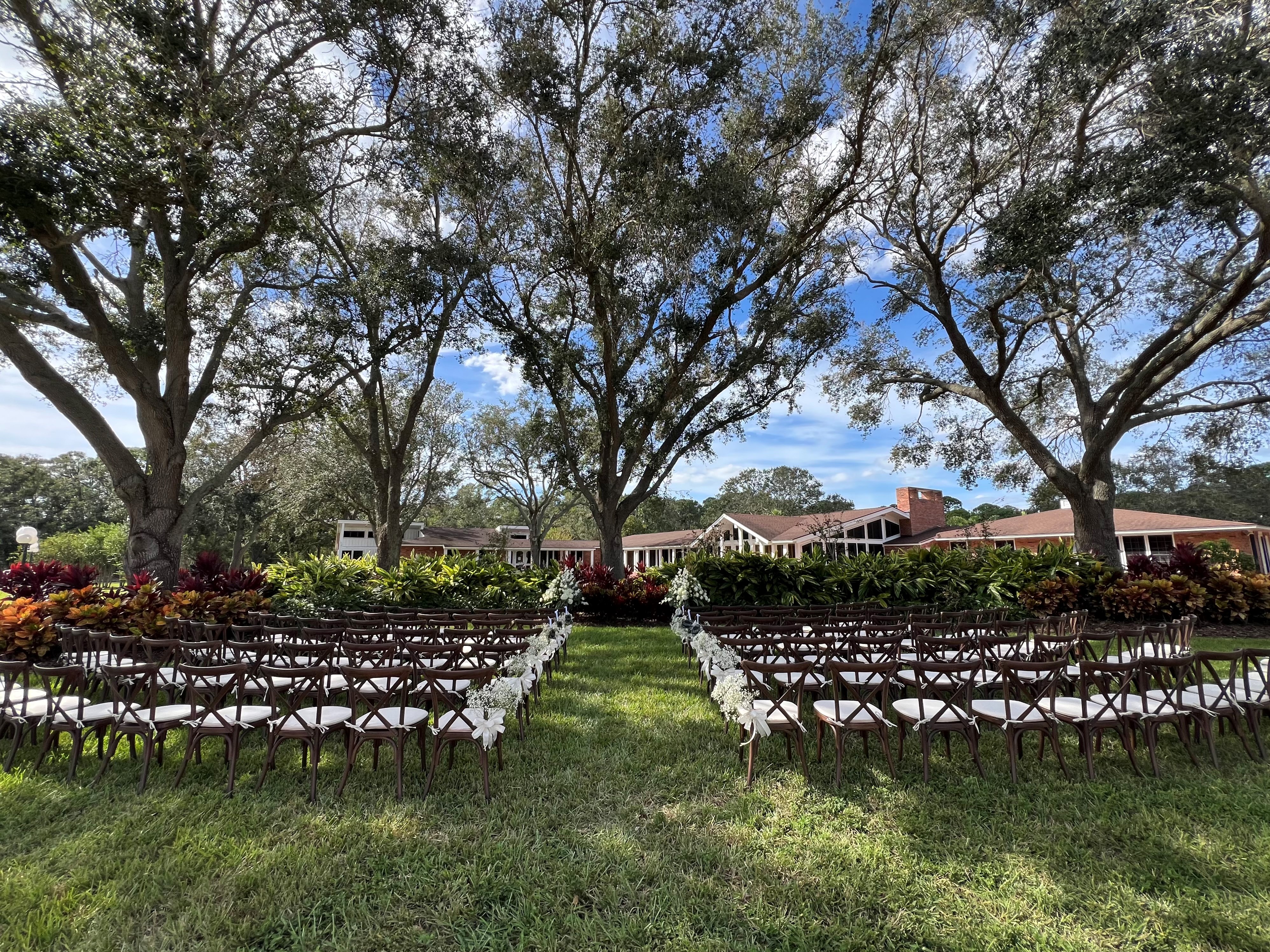 Wedding ceremony set under the trees with cross back chairs