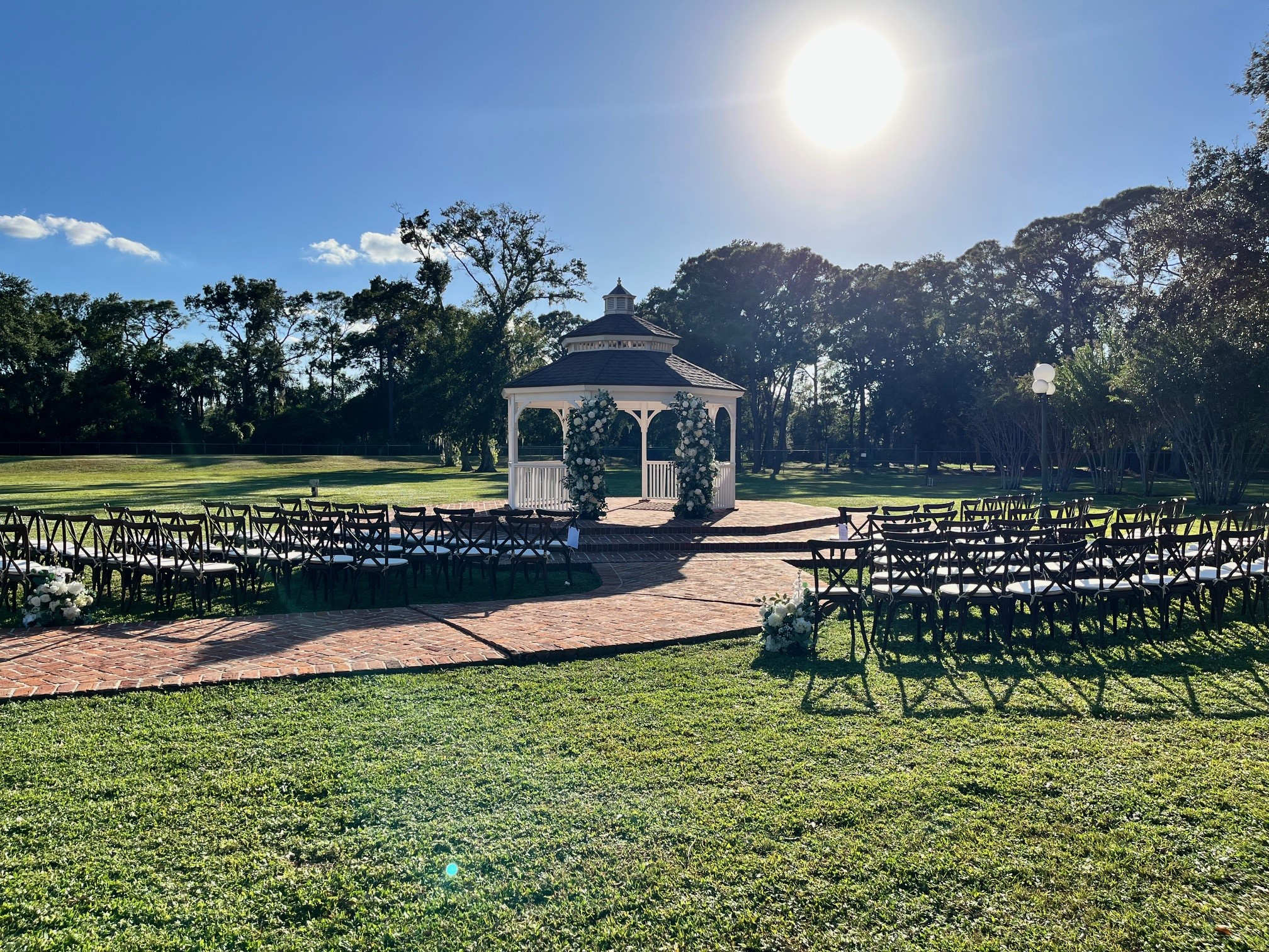 Ceremony set at the gazebo with floral pillars, cross back chairs and matching floral aisle markers
