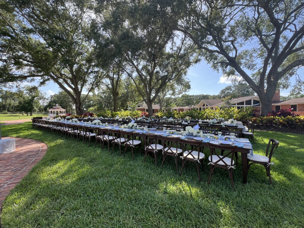 Wedding reception with long farm tables under a canopy of trees