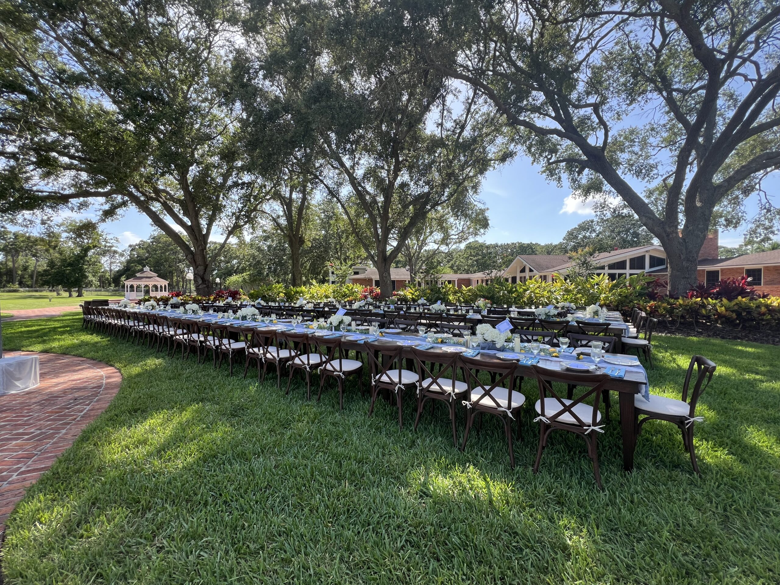 Wedding reception with long farm tables under a canopy of trees 