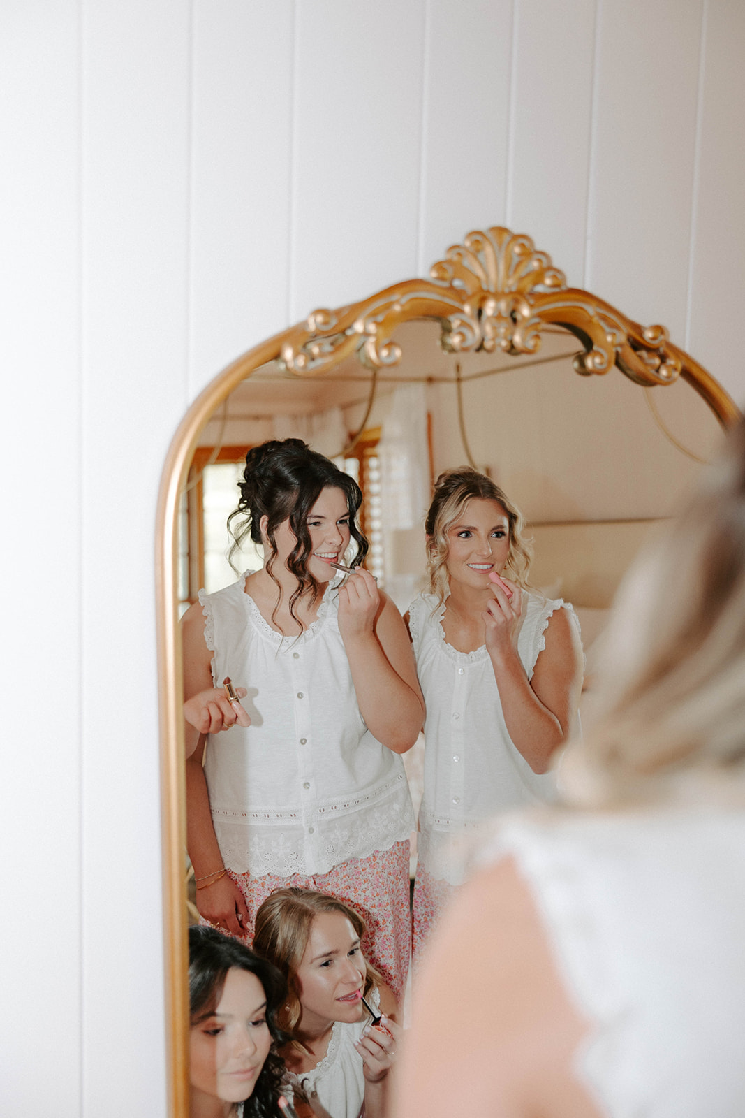 Bride and bridesmaids putting on lipstick in full-length gold mirror