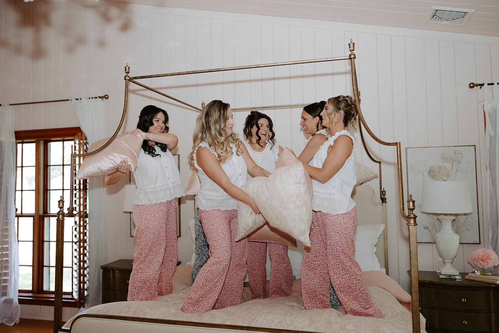 Bride and bridesmaids having pillow fight on bed