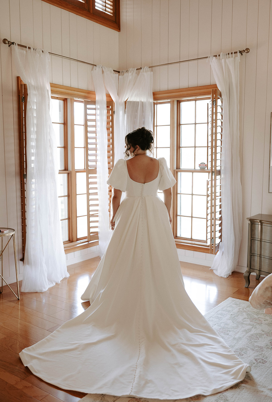 Bride standing in front of windows with wedding dress train spread out
