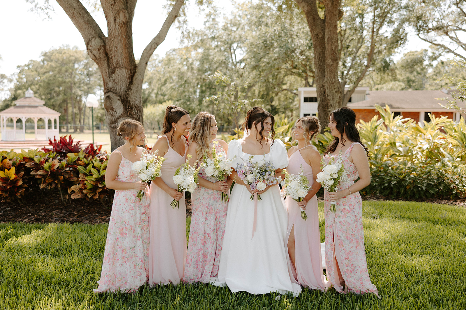 Bride and bridesmaids looking at each other under canopy of oak trees