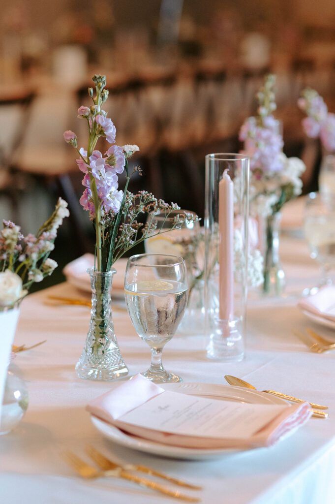 Delicate table setting with blush napkins, gold flatware, bud vases and pink candles